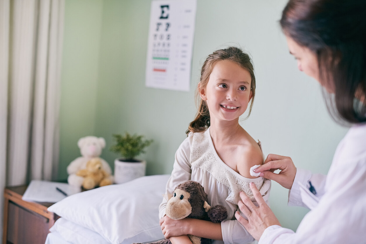 Mädchen mit Kuscheltier in der Hand bekommt Impfung in Oberarm